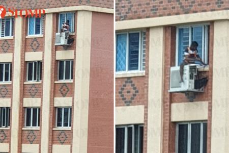 Worker perched atop Tampines air-con compressor on rainy day
