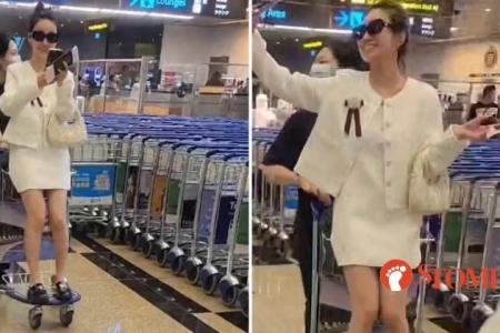 Woman sits on luggage trolley and takes selfie while being pushed around at Changi Airport