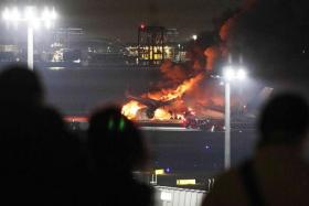 People watch from a viewing area as a Japan Airlines passenger jet (rear) burns on  the tarmac at Haneda Airport in Tokyo, Japan.