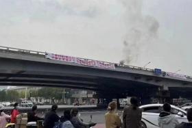 People watch while smoke rises as a banner with a protest message hangs off Sitong Bridge in Beijing on Oct 13. Hundreds of WeChat users have had their accounts blocked after making reference to the demonstration that called for President Xi&#039;s ouster. 