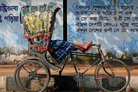 This photograph taken on Dec 13 shows a bicycle rickshaw driver resting in his vehicle by a street kerb in Dhaka. 