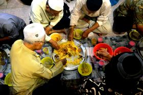 COMMUNITY: Food is shared four to a tray (above) and besides briyani, porridge and fruits are also served. After breaking fast, volunteers such as Mr Shajahan Khan  roll up dining mats and set clean ones for evening prayer. 
