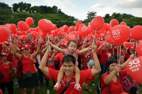 Toddler getting a lift from her father as they help form the SG Heart Map at Bishan-Ang Mo Kio Park on March 14 before the first concert in the park, in the National Parks Board’s SG50 series.
