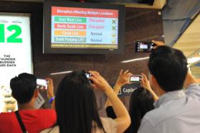 Commuters take photos of a signboard at City Hall MRT station after train services on the East-West and North South lines were disrupted on July 7 - the first time both lines were entirely down. 