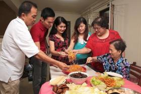 UNITED: Madam Dolly Tan (second from right), tossing yusheng with her family and Ms Cess (in red-black dress) and Mr Anton (in red shirt).