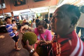 WORTH IT: Retiree Ng Mui Yong (centre) queued under the sun to be first in line to receive free durians from seller Yap Kean Seng.
