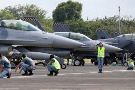 A ground marshall saluting the pilot of an F-16 as he prepares to take off from Tengah Air Base.