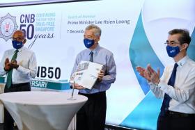 PM Lee holding up a book commemorating the CNB’s 50th anniversary. He is flanked by Minister for Home Affairs and Law K. Shanmugam (left) and CNB director Ng Ser Song.ST PHOTO: KUA CHEE SIONG