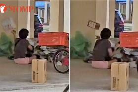 Woman sits in Tampines void deck, sorts parcels by tossing them around