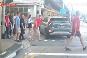 The man in a red shirt taps the car but the driver does not stop.
