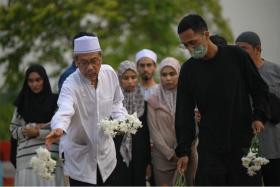 Mr Mohamed Kassim Yusoff (in white) placing flowers on his granddaughter's grave.