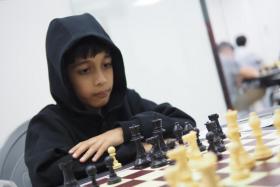 Ashwath Kaushik, 7, has to use a booster cushion to reach the chess board when he was competing in the 2023 Singapore National Chess Championships.