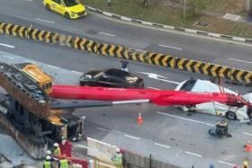 The fallen crane can be seen lying on its side, with its boom stretching across the width of the road and resting on a white van.