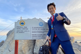 Japanese tailor and adventurer Nobutaka Sada at the summit of Mount Kinabalu, in a business suit.